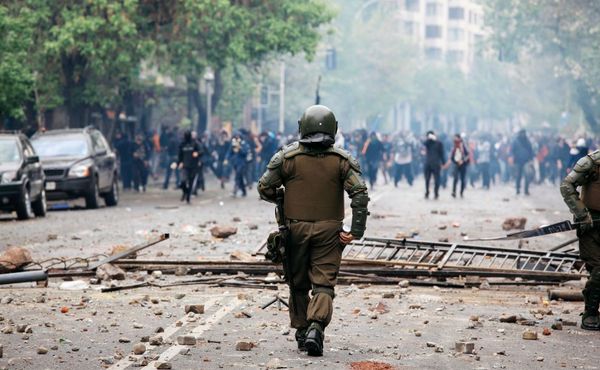 Close up of police officer dealing with rioters in distance