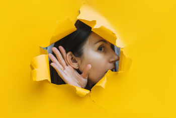 woman listening through yellow wall