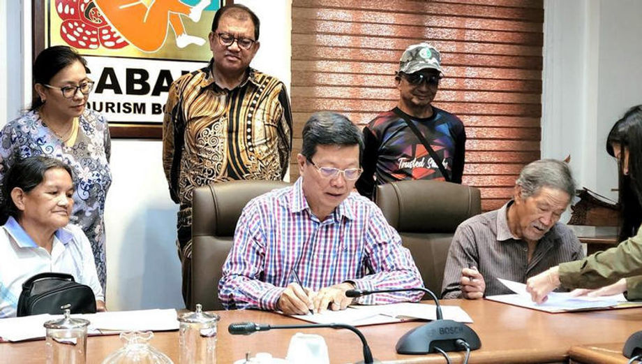 Sabah Tourism Board’s Joniston Bangkuai Noredah Othman (standing, middle) witnessing the signing of MoU between Borneo Eco Tours’ Albert Teo (seated, middle) and villagers.