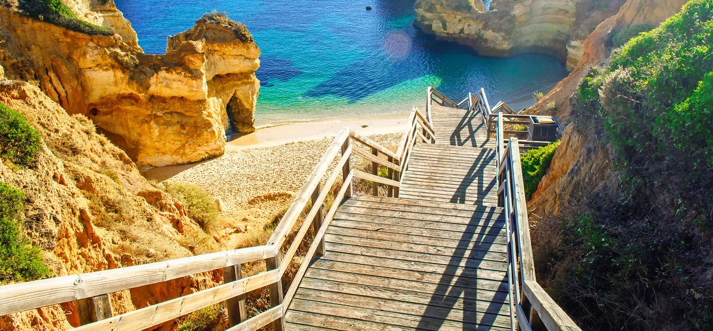 Image: PHOTO: Wooden footbridge to beautiful Praia do Camilo beach near Lagos in Portugal's Algarve region. (photo via samael334 / iStock / Getty Images Plus)