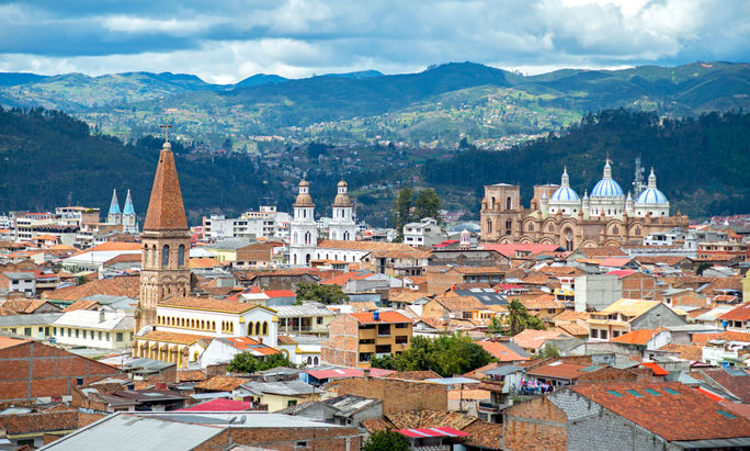 View of the city of Cuenca, Ecuador, with it's many churches and rooftops, on a cloudy day (photo via AlanFalcony / iStock / Getty Images Plus)