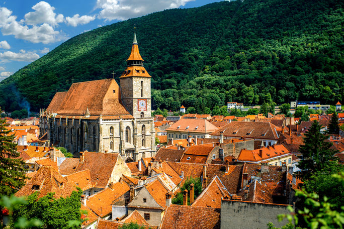 Brasov cityscape with black cathedral and mountain on backround in Romania (photo via RossHelen / iStock / Getty Images Plus)