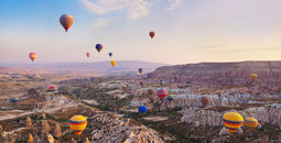 Hot air balloon flying over rock landscape at Cappadocia Turkey (photo via TPopova / iStock / Getty Images Plus)