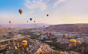 Hot air balloon flying over rock landscape at Cappadocia Turkey (photo via TPopova / iStock / Getty Images Plus)