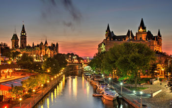 A beautiful warm orange-red glow fills the sky at dusk over Ottawa Canada during a July evening. A small wisp of low level clouds are visible. Parliament Hill, Chateau Laurier hotel and the Rideau Canal a UNSECO world heritage site are in the foreground.