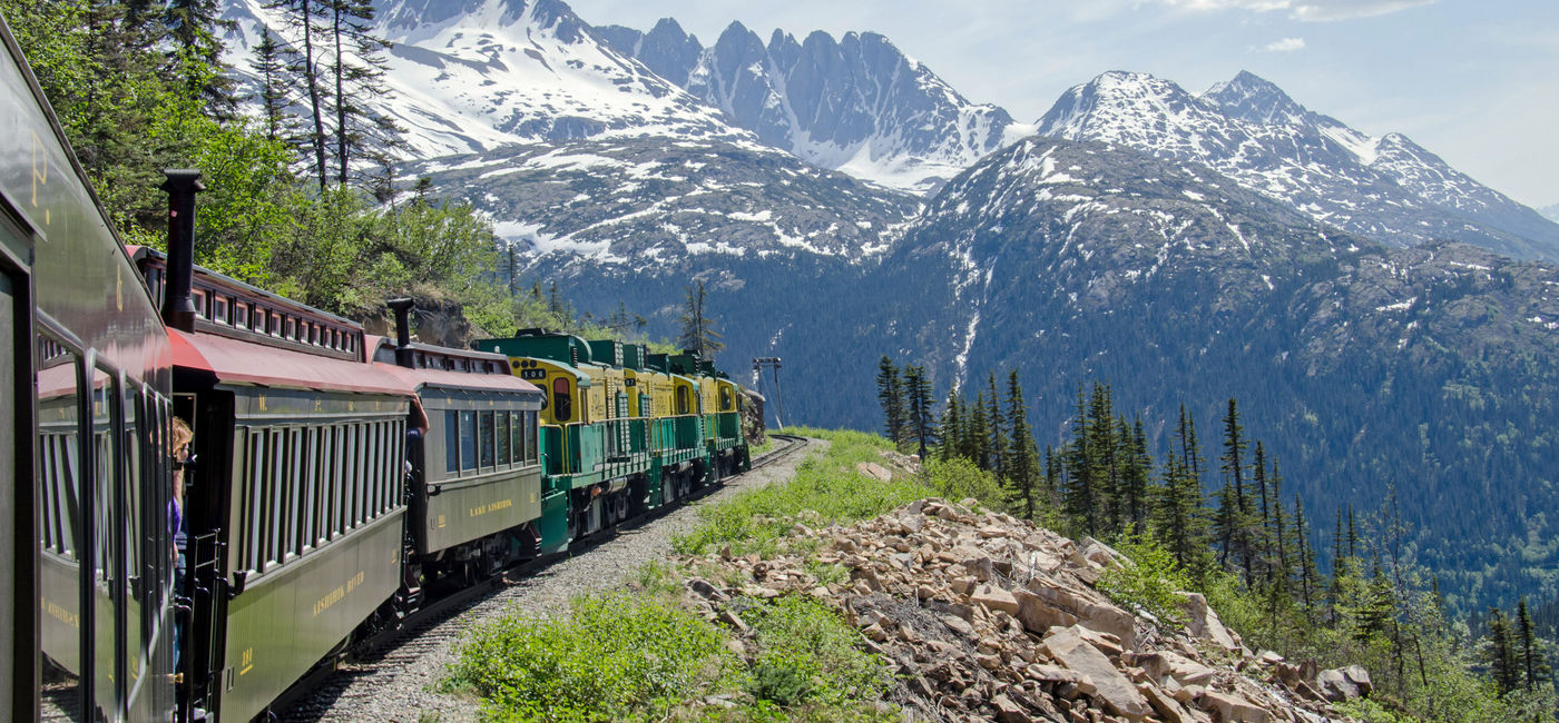Image: PHOTO: White Pass & Yukon Route Railroad travels along the cliffs heading towards Skagway, Alaska. (photo via Chilkoot/iStock/Getty Images Plus)
