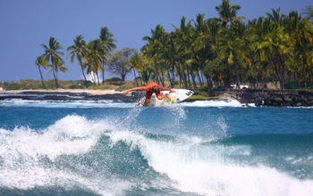 Surfer flying above wave crest with palm trees in background