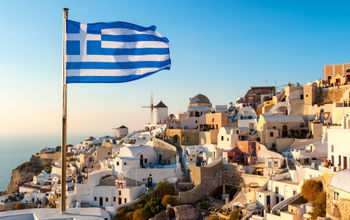 The Greek flag flying at sunset in the town of Oia in Santorini, Greece.