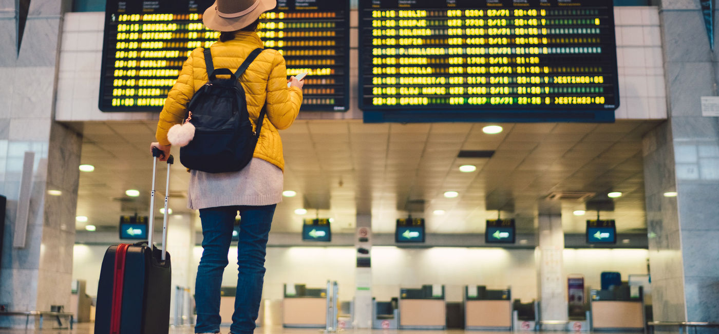 Image: Young woman at airport checking flight departures. (Photo via martin-dm / Getty Images / E+)