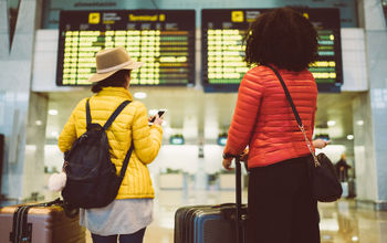 Tourists at the airport waiting for the flight to be announced on the arrival departure board