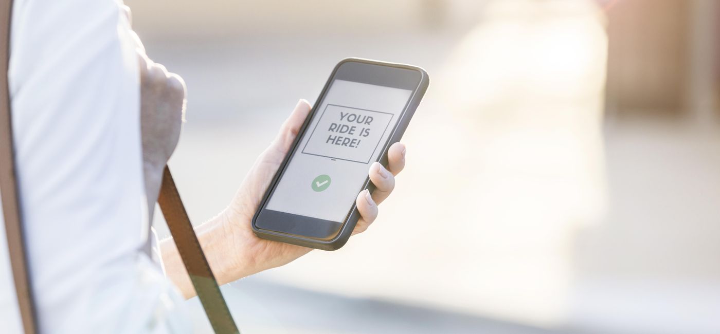 Image: Confident businesswoman uses ride share app on her smart phone. The message on the phone indicates that her ride has arrived. (Photo via asiseeit / iStock / Getty Images Plus)