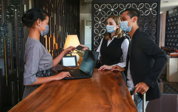 Guests and receptionist wearing face masks at a hotel check-in counter.