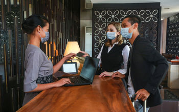Guests and receptionist wearing face masks at a hotel check-in counter.