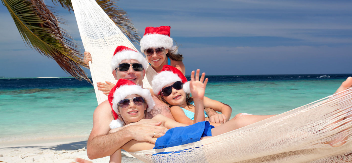 Image: Family spending their winter vacation in a warm-weather destination and sporting Santa hats. (Photo via iStock / Getty Images / amriphoto)