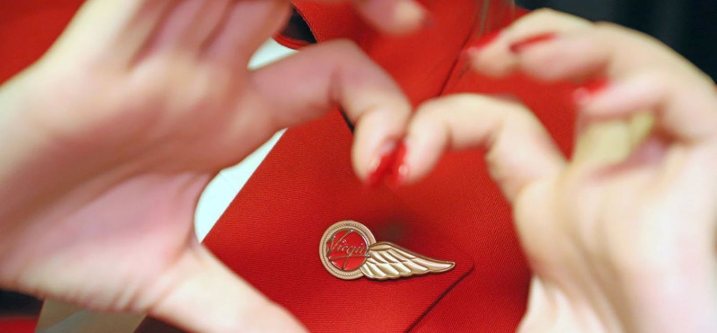 Image: A woman forms the shape of a heart with her hands around a Virgin Atlantic pin. (photo via Virgin Atlantic) ((photo via Virgin Atlantic))
