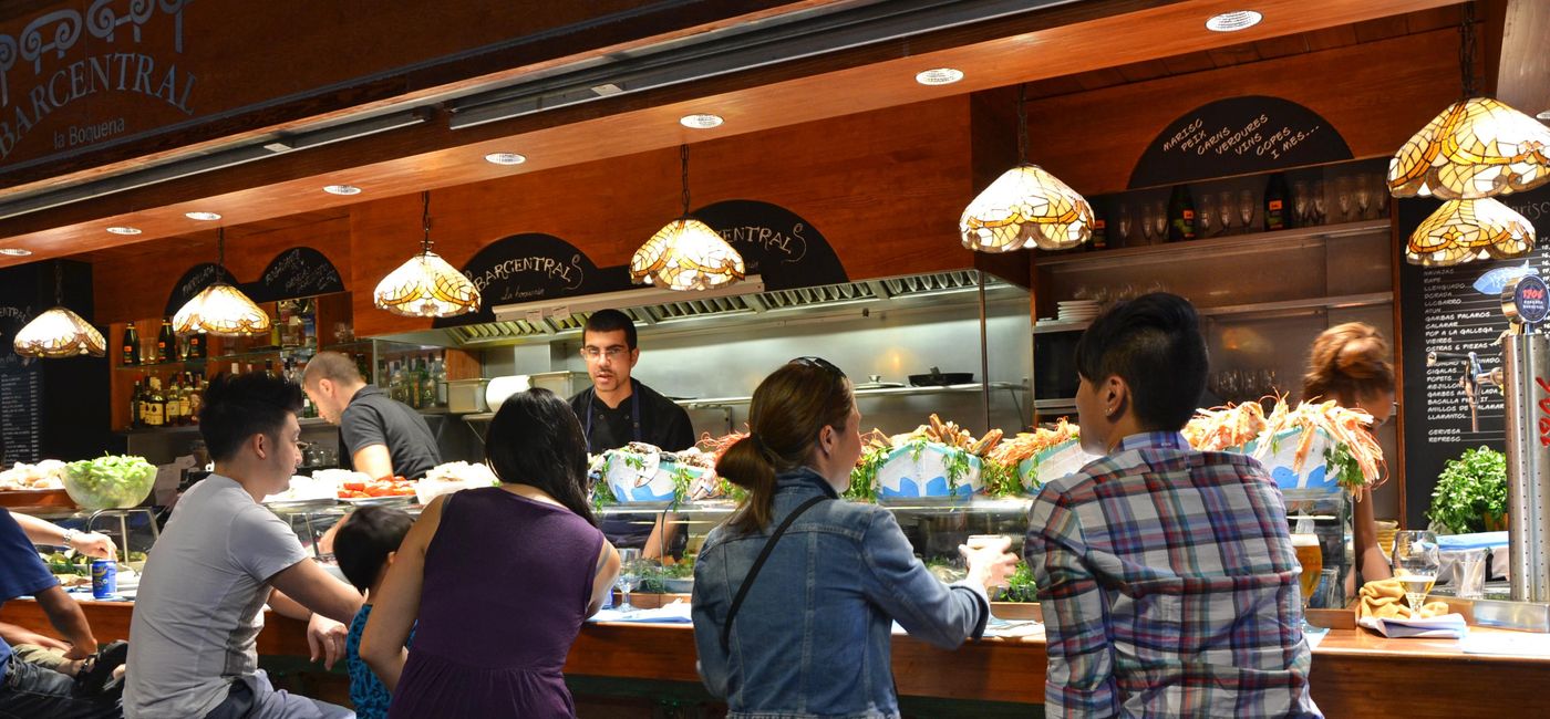 Image: Customers at a tapas bar at La Boqueria market in Barcelona, Spain. (photo via Maisna/iStock Editorial/Getty Images Plus)