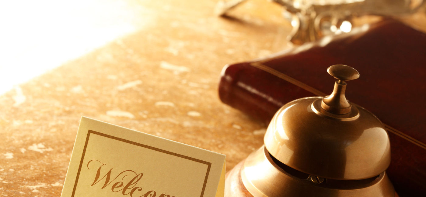 Image: Welcome card and service bell sitting on a hotel reception desk. (photo via iStock/E+/DNY59)