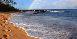 'Aloha' on Hawaiian beach beneath a rainbow.
