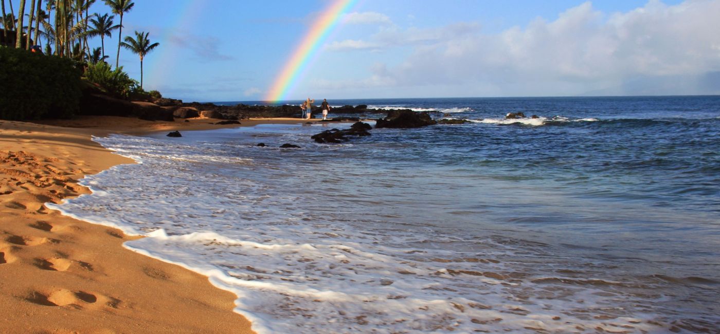 Image: 'Aloha' written on a sandy Hawaiian beach beneath a rainbow. (Photo via iStock/Getty Images Plus/ejs9)