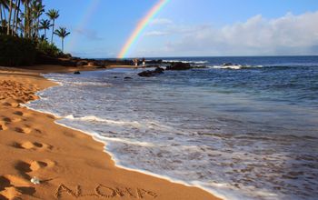 'Aloha' on Hawaiian beach beneath a rainbow.