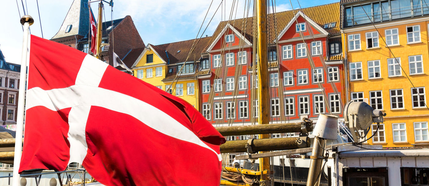Denmark's national flag flying in the foreground of Copenhagen's famous old Nyhavn port.