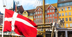 Denmark's national flag flying in the foreground of Copenhagen's famous old Nyhavn port.