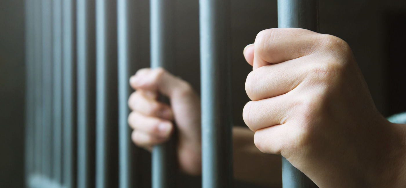 Image: Person in prison behind steel bars. (Photo via iStock/Getty Images Plus/Rattankun Thongbun)