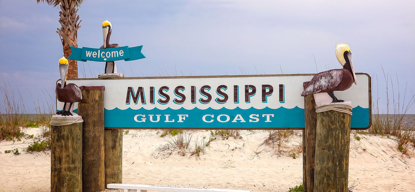 Image: PHOTO: Welcome to Mississippi Gulf Coast Sign on Beach. (photo via CrackerClips / iStock / Getty Images Plus)