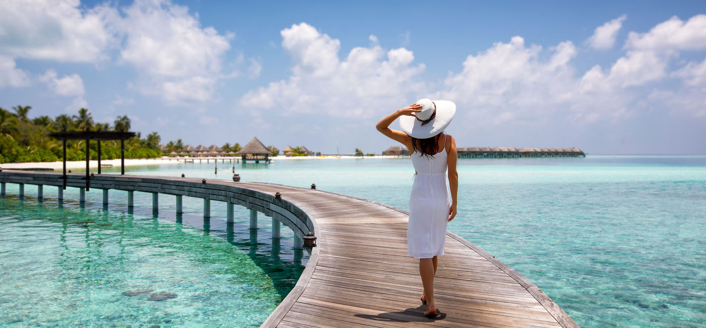 Image: Woman walking along a wooden jetty in the Maldives. (photo via iStock / Getty Images Plus / SHansche)