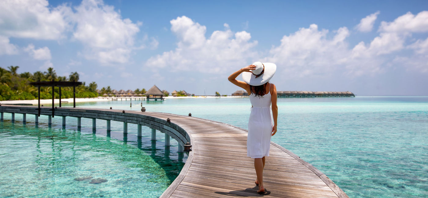 Photo: Woman walking along a wooden jetty in the Maldives. (photo via iStock / Getty Images Plus / SHansche)