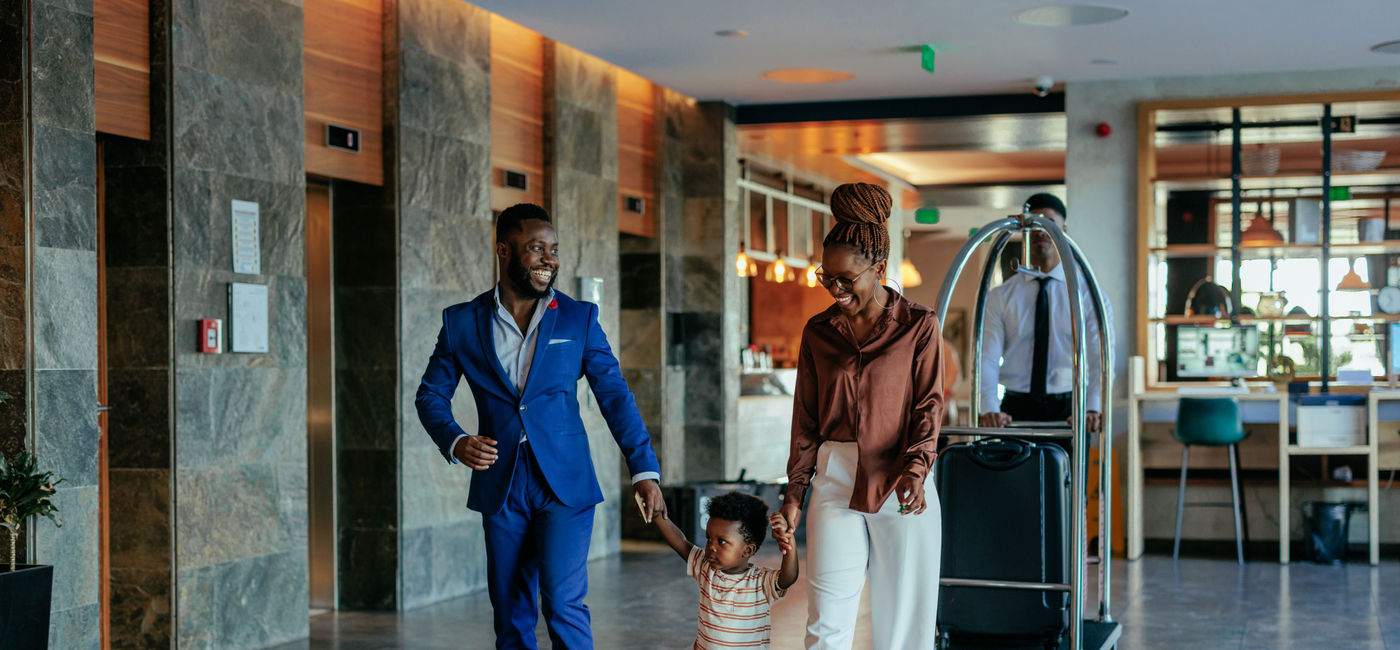 Image: An African American family walking through the lobby of luxury hotel (Photo Credit: Dimensions / Getty Images)