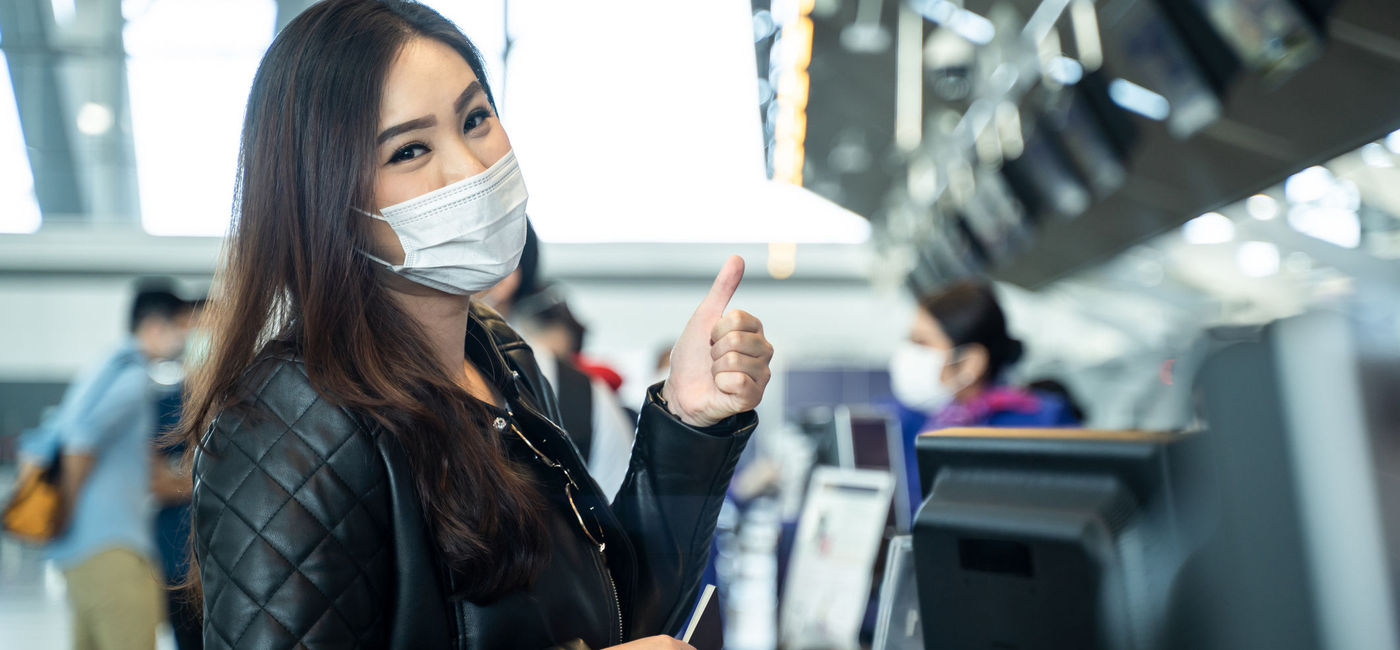 Image: PHOTO: Young woman wearing a mask at airport check-in. (Photo via iStock/Getty Images Plus/Kiwis)