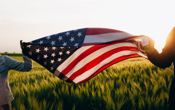 Hands holding American flag in a wheat field on Independence Day.