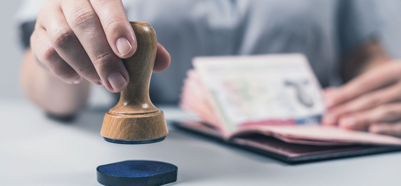 Image: Customs and Immigration Control officer stamping a passport. (Photo via iStock/Getty Images Plus/FTiare)