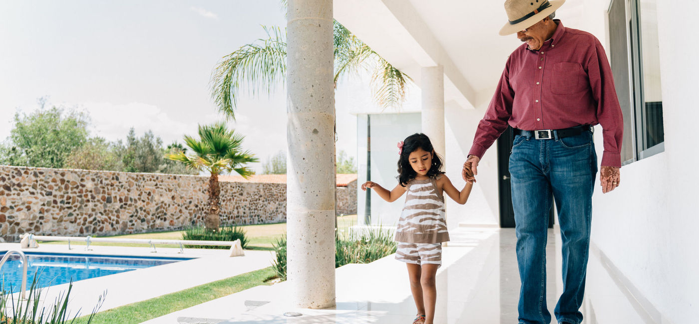 Image: Grandfather and granddaughter walking poolside at a luxury villa. (photo via ferrantraite / E+)