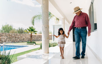Grandfather and granddaughter walking poolside at a luxury villa.
