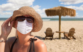Woman vacationing on a sandy beach wearing a mask.