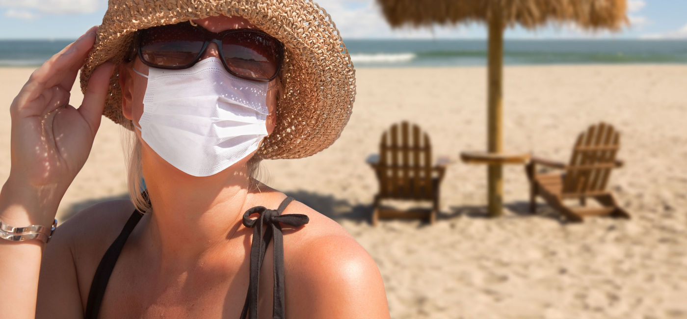 Image: Woman vacationing on a sandy beach wearing a mask. (Photo via iStock/Getty Images Plus/Feverpitched)