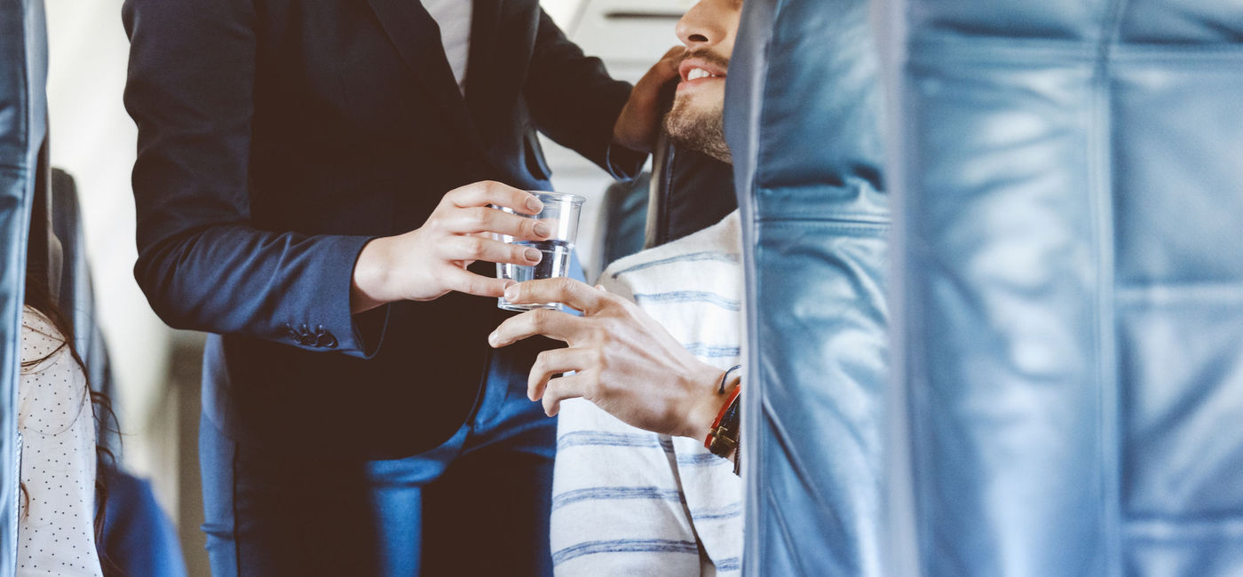 Image: Airline hostess serving water to a passenger. (photo via Getty Images E+ / izusek)