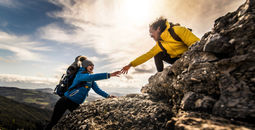 People helping each other hike up a mountain at sunrise.