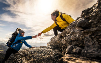 People helping each other hike up a mountain at sunrise.