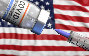 COVID-19 vaccine vial with U.S. flag in the background.