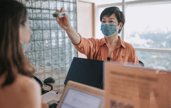 Hotel receptionist running a temperature check on arriving guest