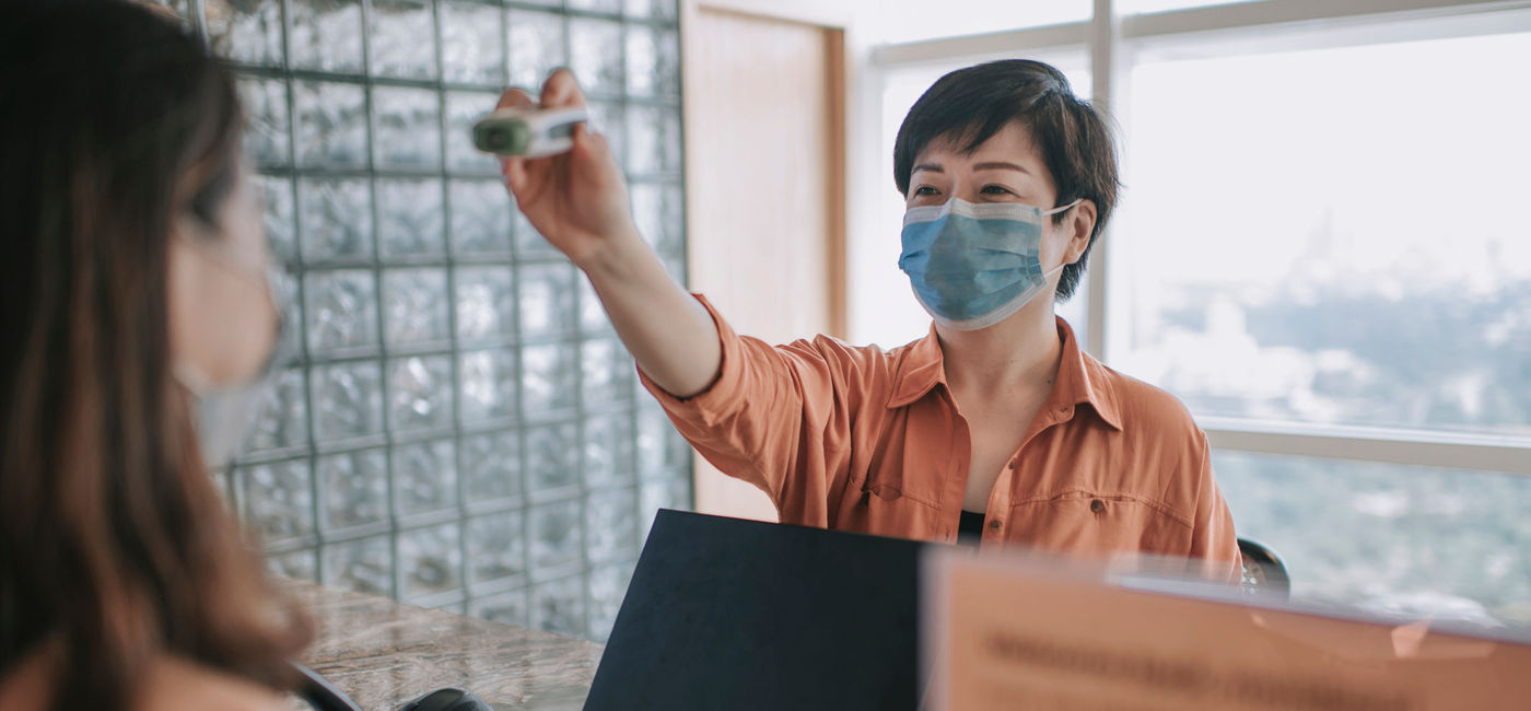 Image: PHOTO: Hotel receptionist running a temperature check on arriving guest. (photo via chee gin tan/E+)