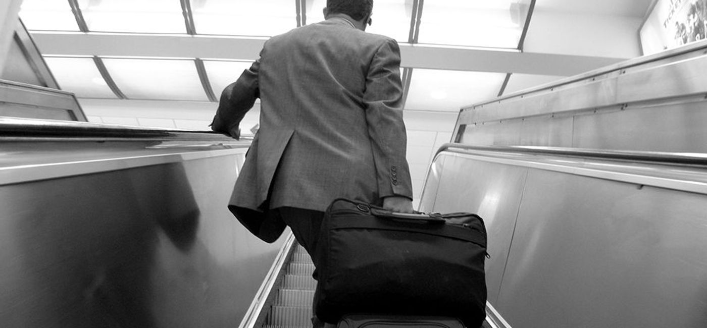 Image: PHOTO: Business traveler lugging a suitcase up an escalator at an airport. (photo via Flickr/frankieleon)