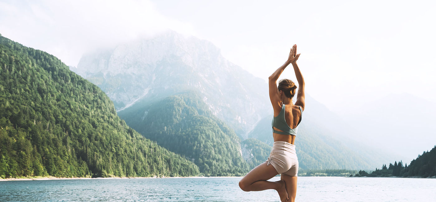 Image: A traveler doing a yoga pose near the water. (photo via Wellness Travel University)