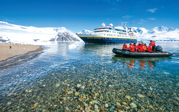 A zodiac cruises in front of a Lindblad Expeditions vessel.