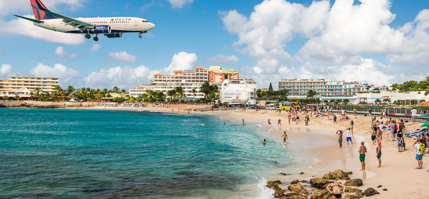 Image: Delta flight approaches St Maarten's Princess Juliana Airport above onlookers on Maho Beach. (photo via SeanPavonePhoto/iStock Editorial/Getty Images Plus)