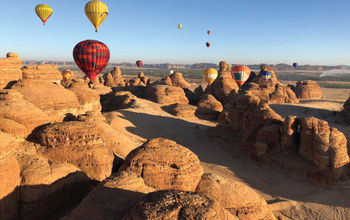 Hot air balloons floating above a Saudi Arabian landscape.
