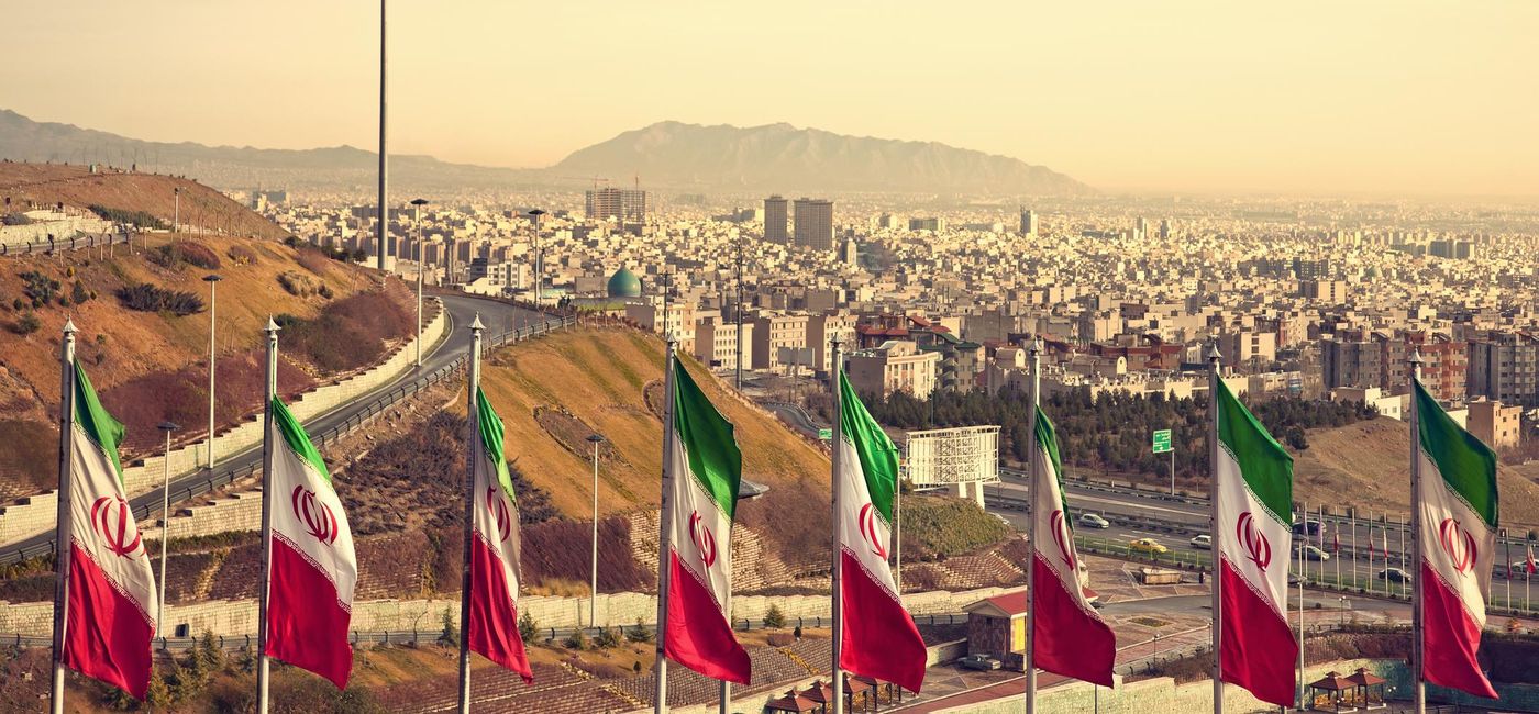 Image: PHOTO: Row of Iran Flags in front of Tehran skyline. (photo via BornaMir/iStock/Getty Images Plus)